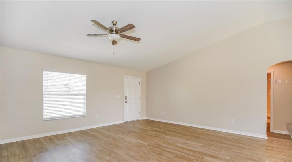 An empty living room features light wood-look flooring, beige walls, a ceiling fan, and a door — 2656 W CASTANIA DRIVE, DUNNELLON, FL