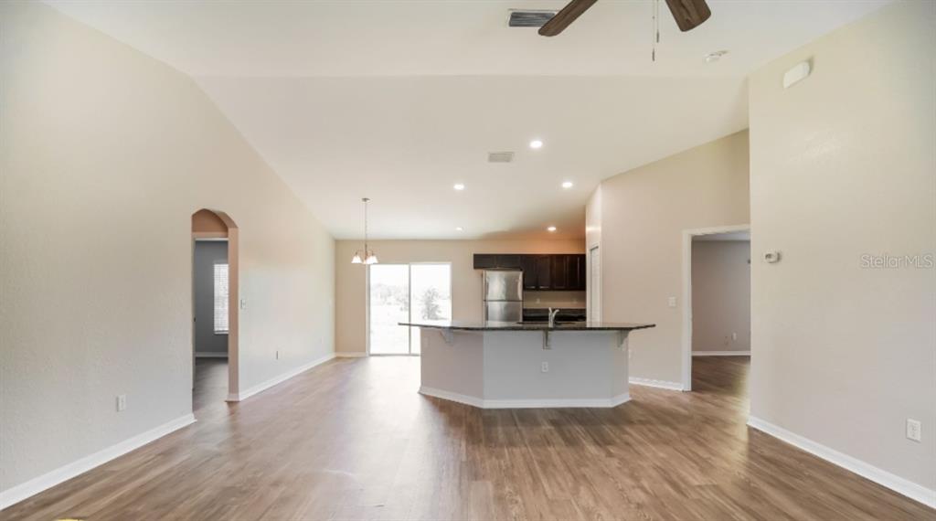 An open-concept kitchen and living area features wood-look flooring, a kitchen island, and vaulted ceilings — 2656 W CASTANIA DRIVE, DUNNELLON, FL