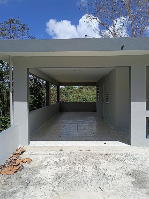 A covered, tiled patio area is attached to the side of a gray concrete house — 156 BO. BAYAMONCITO, AGUAS BUENAS, PR