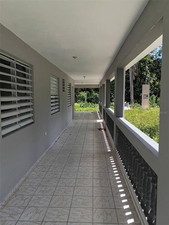 A long, covered outdoor balcony with tiled flooring, gray walls, and a decorative concrete railing — 156 BO. BAYAMONCITO, AGUAS BUENAS, PR