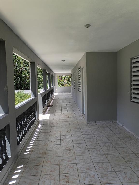 A long, covered outdoor balcony with tiled flooring, gray walls, and a decorative railing — 156 BO. BAYAMONCITO, AGUAS BUENAS, PR