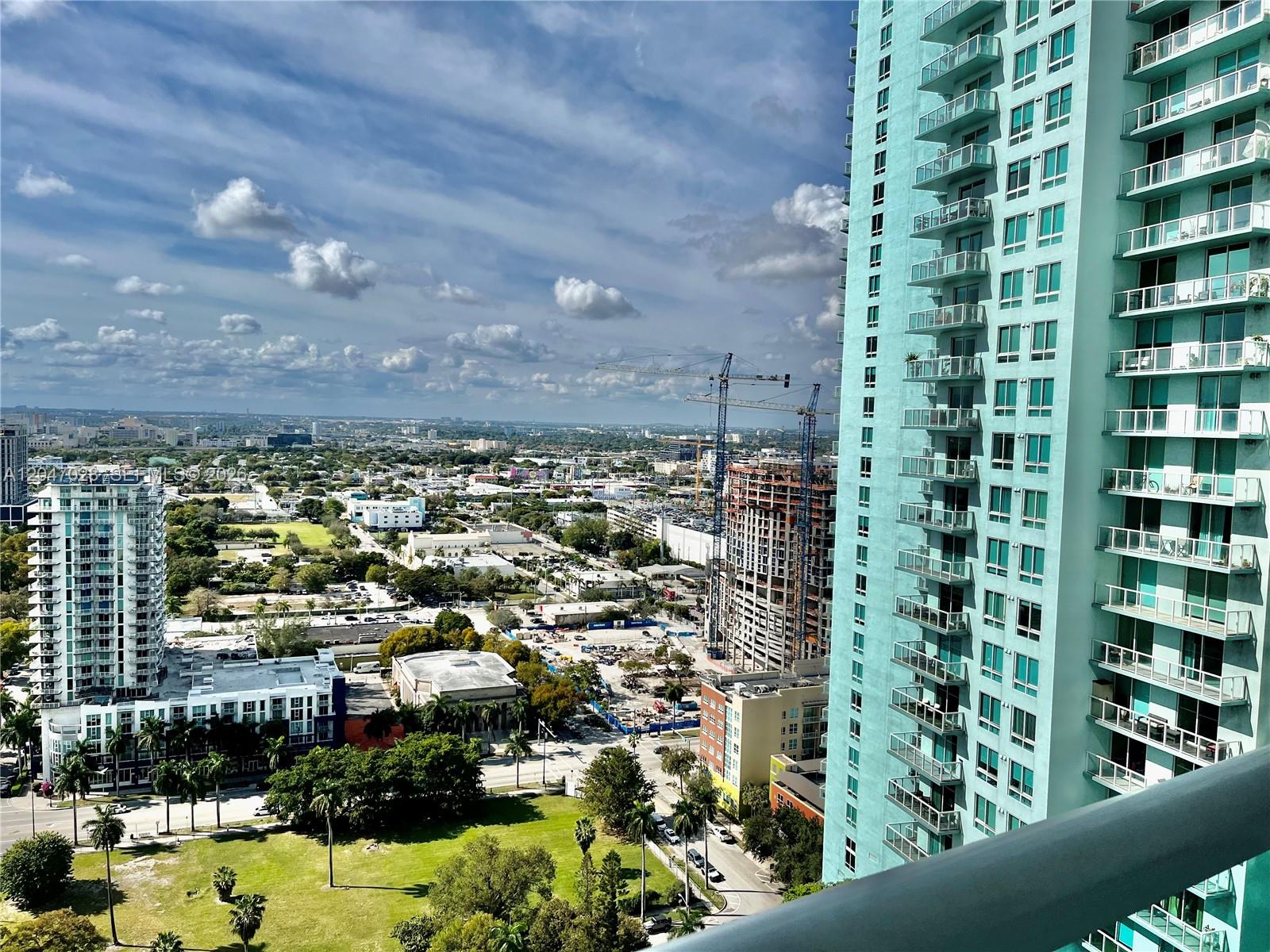 An elevated view shows a city skyline with high-rise buildings, construction cranes, and green spaces — MIAMI, FL