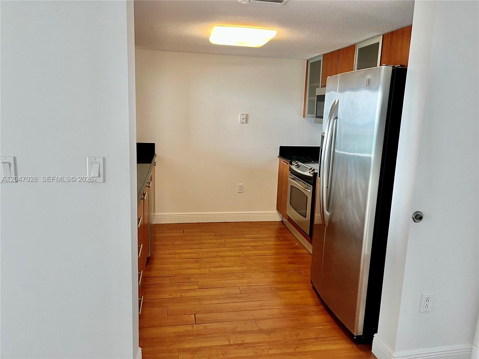 A galley kitchen features wood cabinets, stainless steel appliances, black countertops, and hardwood flooring — MIAMI, FL