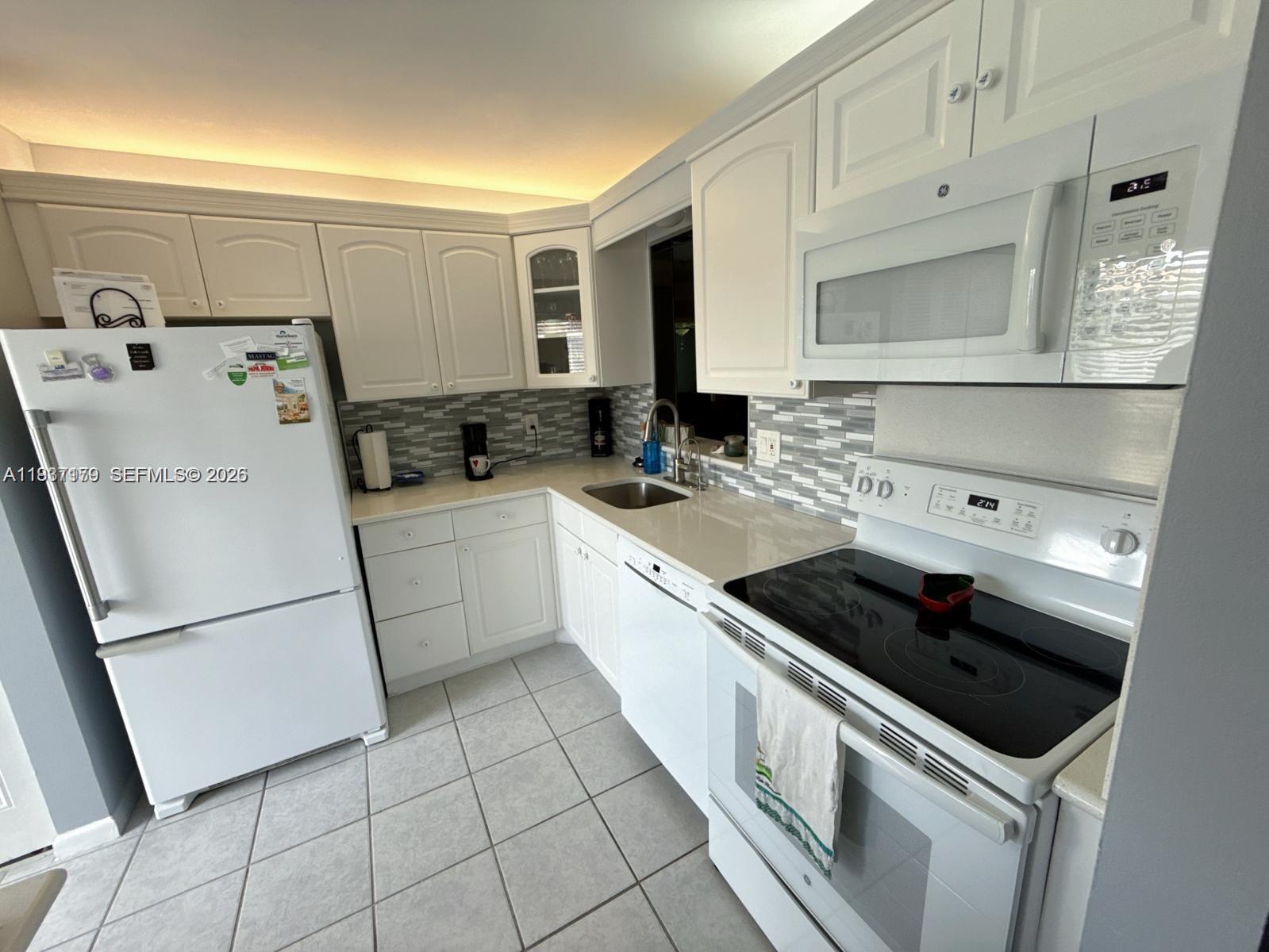A white kitchen features tile flooring, white cabinetry, a glass-tiled backsplash, and stainless steel appliances — 6720 Moonlit Dr, Delray Beach FL 33446, DELRAY BEACH, FL