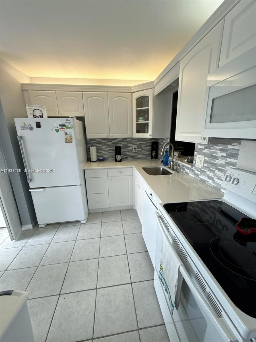 A kitchen features white cabinets, a white refrigerator, a glass-top stove, and tiled flooring — 6720 Moonlit Dr, Delray Beach FL 33446, DELRAY BEACH, FL