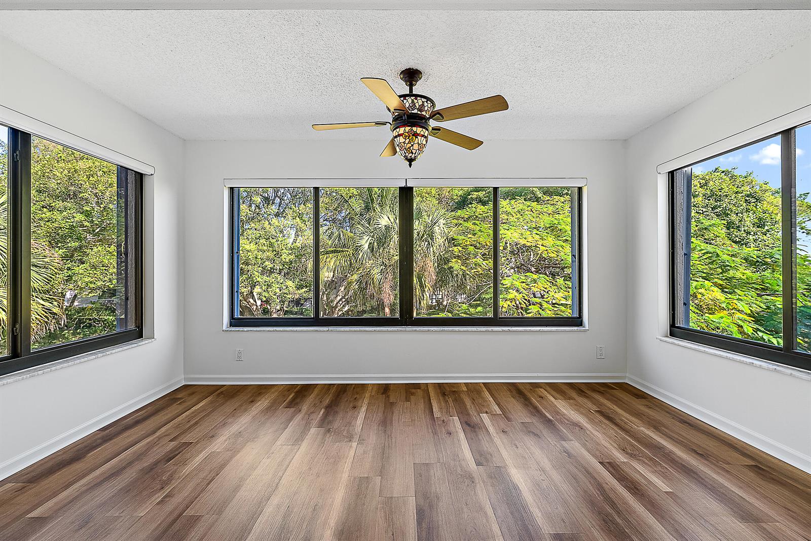 An empty living room features white walls, wood-look flooring, and large windows overlooking trees — 300 N Highway A1a # 303g, Jupiter FL 33477, JUPITER, FL