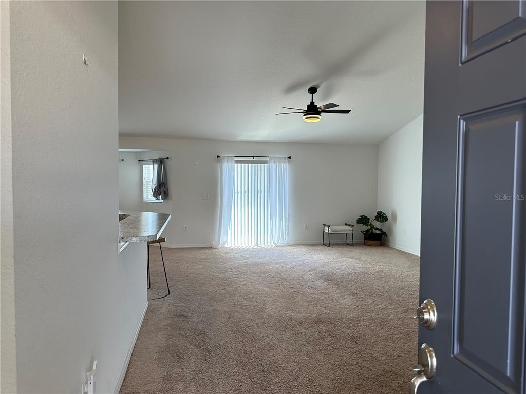 An interior view shows a carpeted living room with a ceiling fan and sliding glass doors — 1116 CALOOSA RIDGE WAY, BABSON PARK, FL