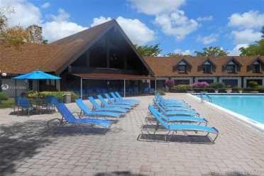 A swimming pool sits beside a large building with a brown roof and lounge chairs — 3760 Inverrary Drive # 2h, Lauderhill FL 33319, LAUDERHILL, FL