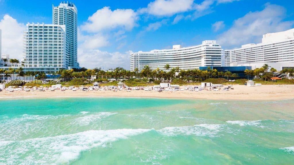 An exterior view of a beach with white sand, turquoise water, and large resort buildings — 4391 Collins Ave # 419, Miami Beach FL 33140, MIAMI BEACH, FL
