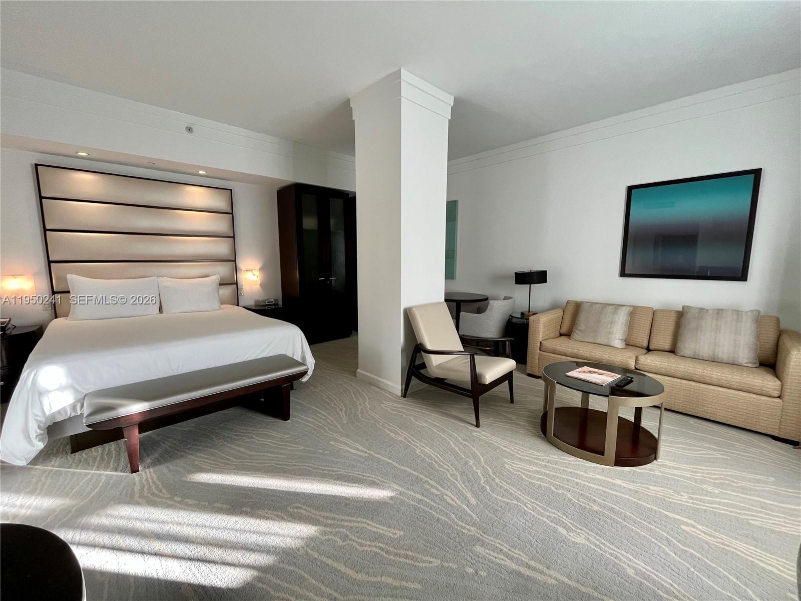 A hotel suite features a king bed, a sitting area with a sofa, and carpeted floors — 4391 Collins Ave # 419, Miami Beach FL 33140, MIAMI BEACH, FL