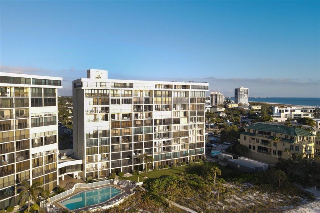 An aerial view shows two tall residential buildings with balconies, a swimming pool, and landscaping — 20 WHISPERING SANDS DRIVE UNIT 903, SARASOTA, FL
