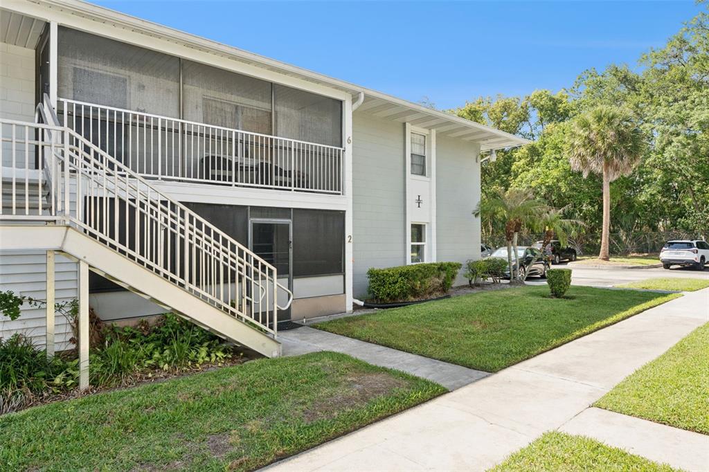 A two-story apartment building features exterior staircases, screened-in balconies, and a landscaped lawn — 700 E AIRPORT BLVD UNIT I2, SANFORD, FL