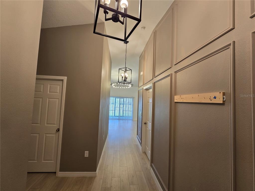 A hallway features light wood-look tile flooring, paneled walls, and two hanging lantern-style light fixtures — 2441 OAKWOOD LANE, DAVENPORT, FL