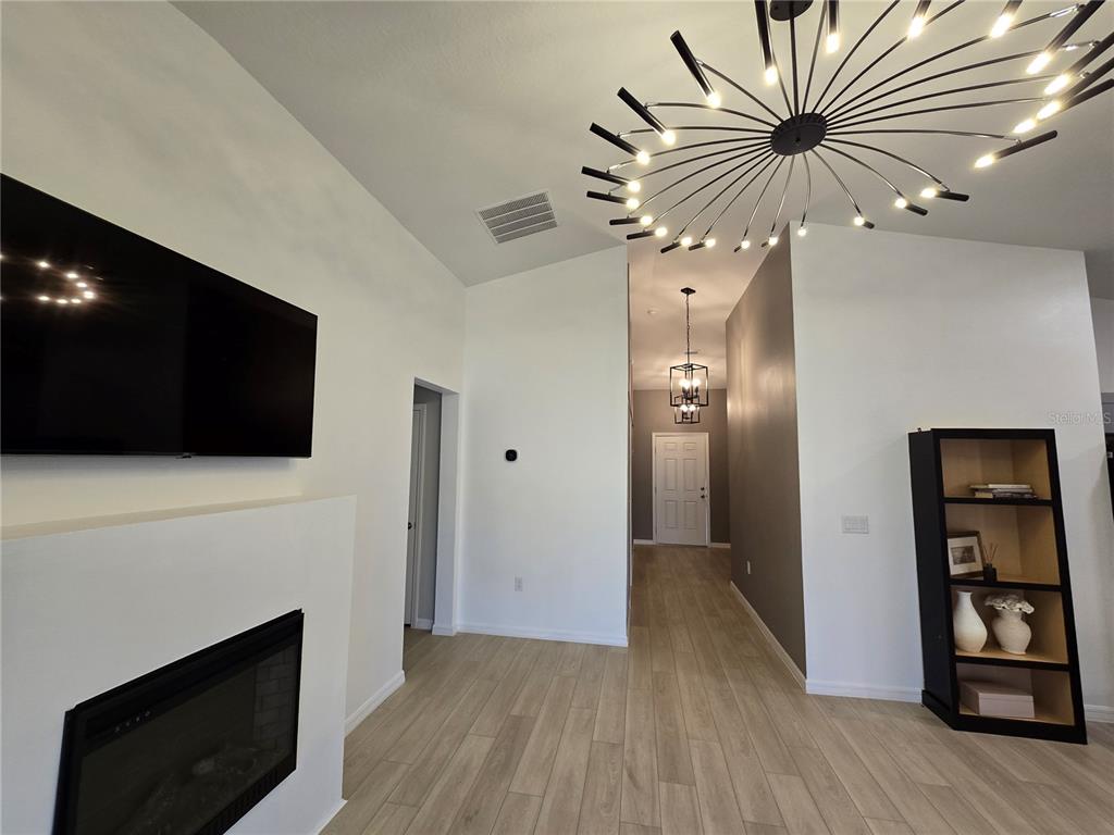 A living room features a fireplace, a large modern chandelier, and light wood-look flooring — 2441 OAKWOOD LANE, DAVENPORT, FL