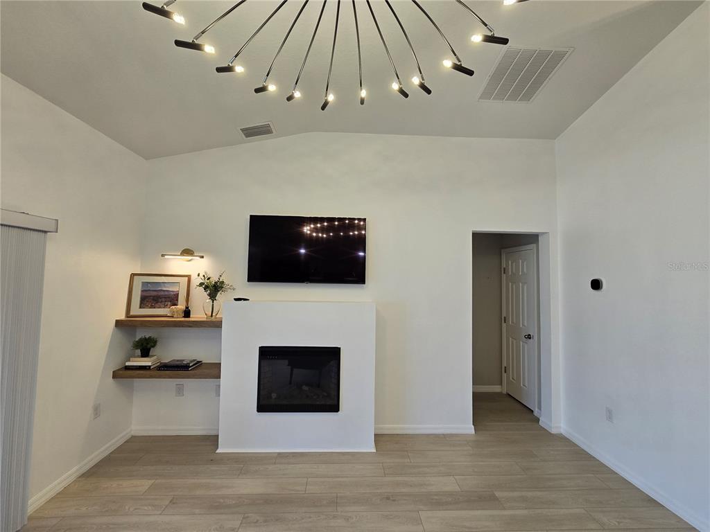 A living room features a fireplace, wall-mounted television, floating shelves, and a modern chandelier — 2441 OAKWOOD LANE, DAVENPORT, FL