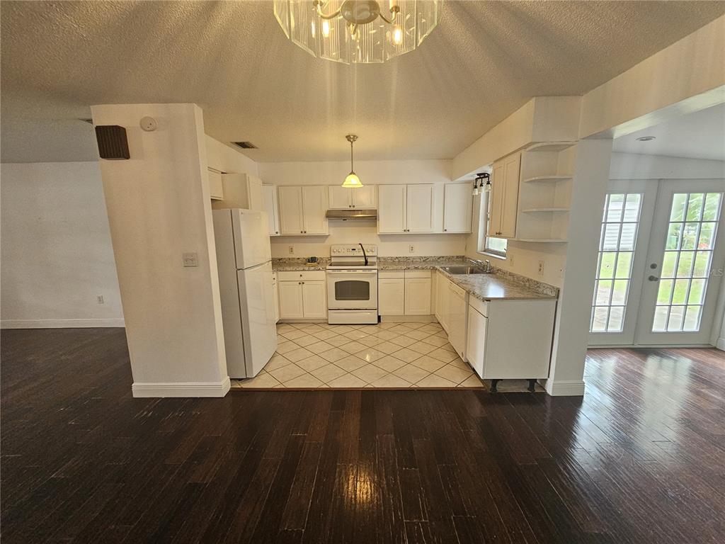 A kitchen with white cabinets, laminate countertops, and tile flooring opens to a dark-wood floor — 26 LAKE COURT LOOP, OCALA, FL
