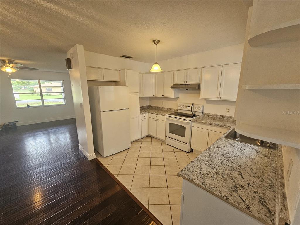 A kitchen with white cabinets, granite countertops, and tiled flooring adjacent to a living area — 26 LAKE COURT LOOP, OCALA, FL