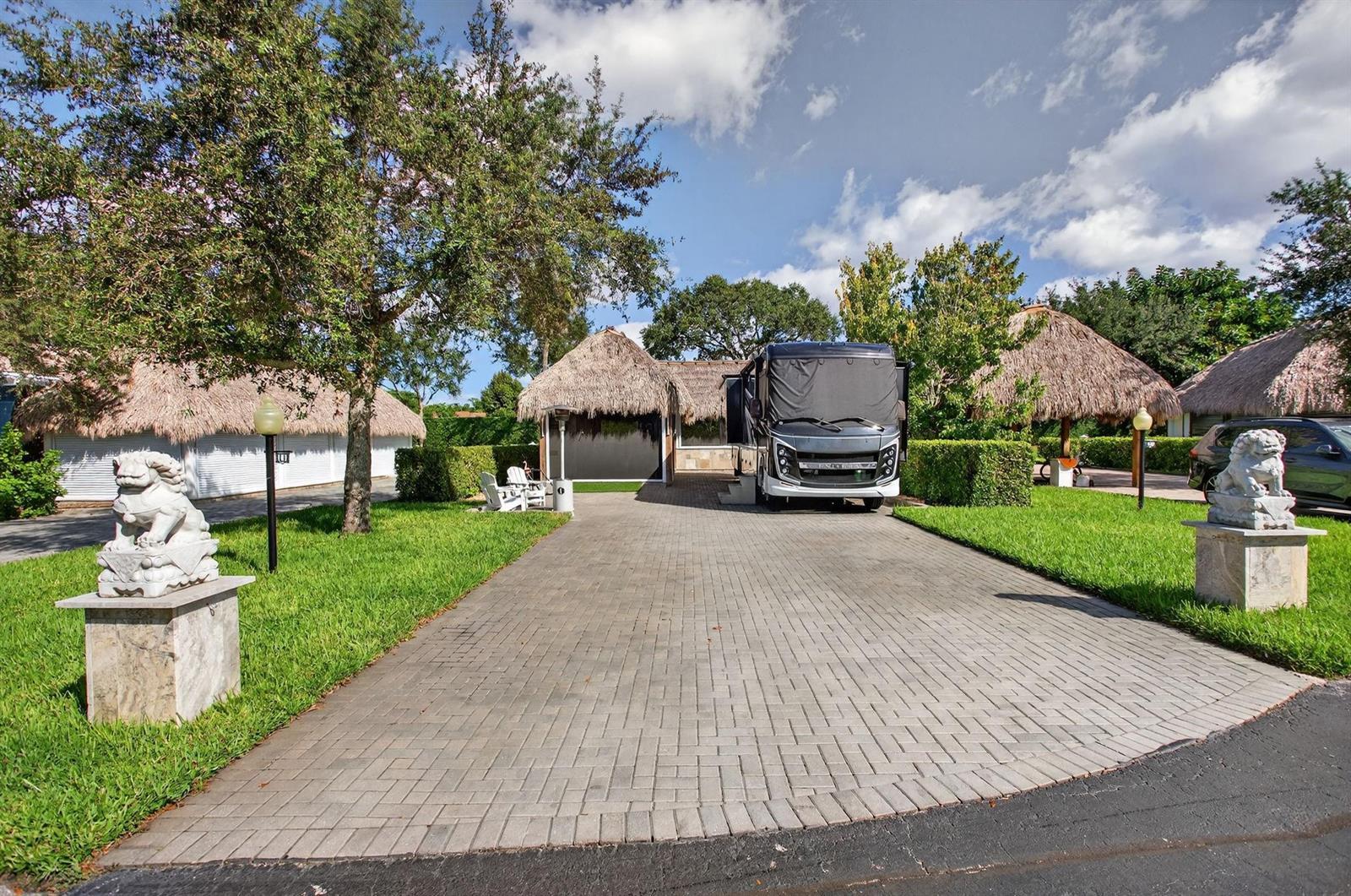 A paved driveway leads to a motorhome parked under a thatched-roof structure with stone statues — 161 N Cortez Drive # 161, Margate FL 33068, MARGATE, FL