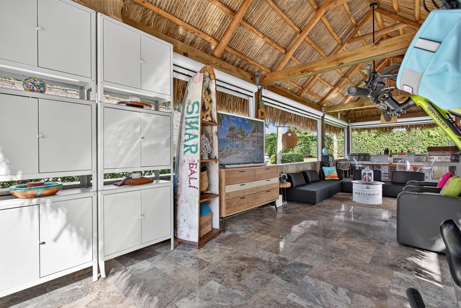 An open-air patio features a thatched roof, stone flooring, white storage cabinets, and lounge furniture — 161 N Cortez Drive # 161, Margate FL 33068, MARGATE, FL