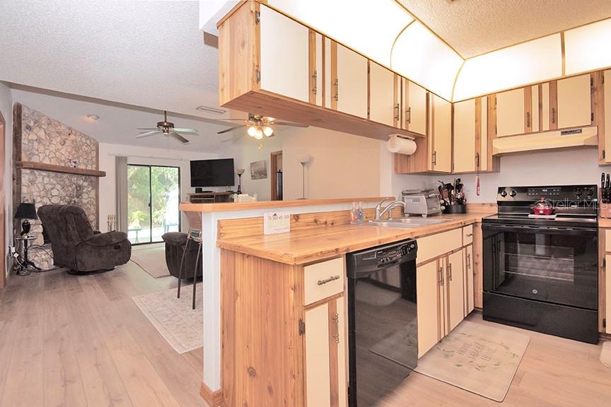 A kitchen with wood-trimmed cabinets and a breakfast bar overlooks a living room with stone — 823 SUGAR HOUSE BOULEVARD, PORT ORANGE, FL