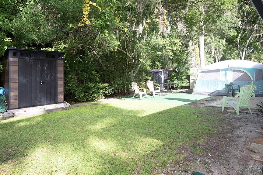 A backyard features a storage shed, a tent, and lawn chairs on a grassy lot — 823 SUGAR HOUSE BOULEVARD, PORT ORANGE, FL