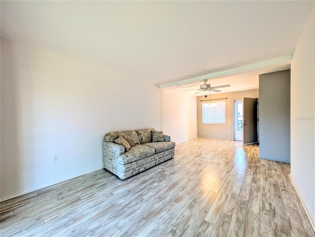 A living room features light wood-look flooring, a patterned sofa, and a ceiling fan — 2319 CANAL DRIVE UNIT F26, BRADENTON, FL