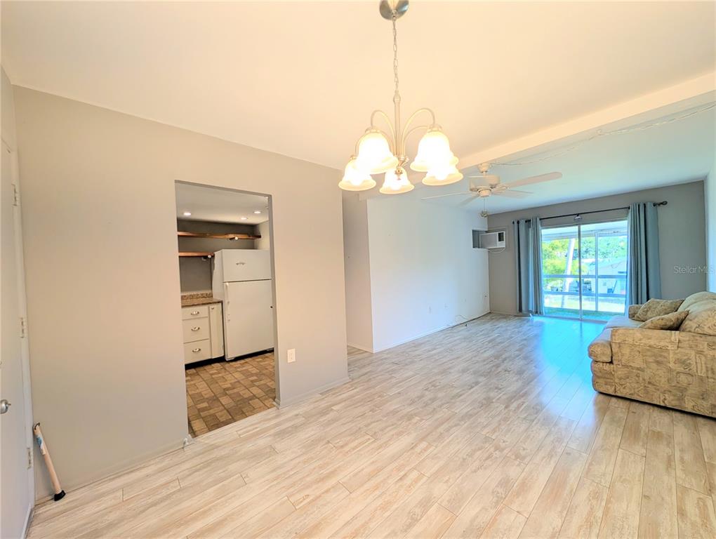 A living room with light wood-look flooring leads to a kitchen and a sliding glass door — 2319 CANAL DRIVE UNIT F26, BRADENTON, FL