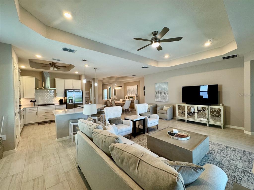An open-concept living room and kitchen feature light tile floors, white cabinetry, and neutral furniture — 19140 CHERRYSTONE WAY, LAKEWOOD RANCH, FL