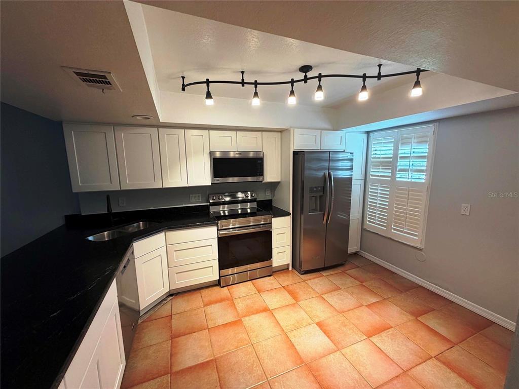 A kitchen features white cabinets, black countertops, stainless steel appliances, and orange tiled flooring — 5291 INDIAN LAUREL COURT, ORLANDO, FL