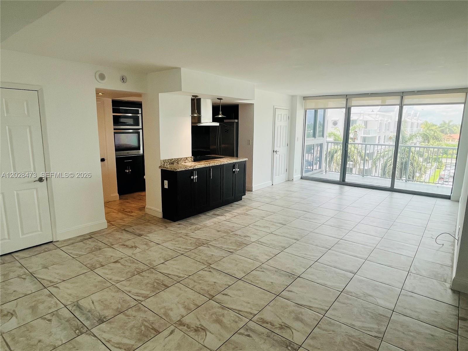 An open-concept living area features tile flooring, a kitchen with dark cabinets, and balcony access — 2655 Collins Ave # 602, Miami Beach FL 33140, MIAMI BEACH, FL
