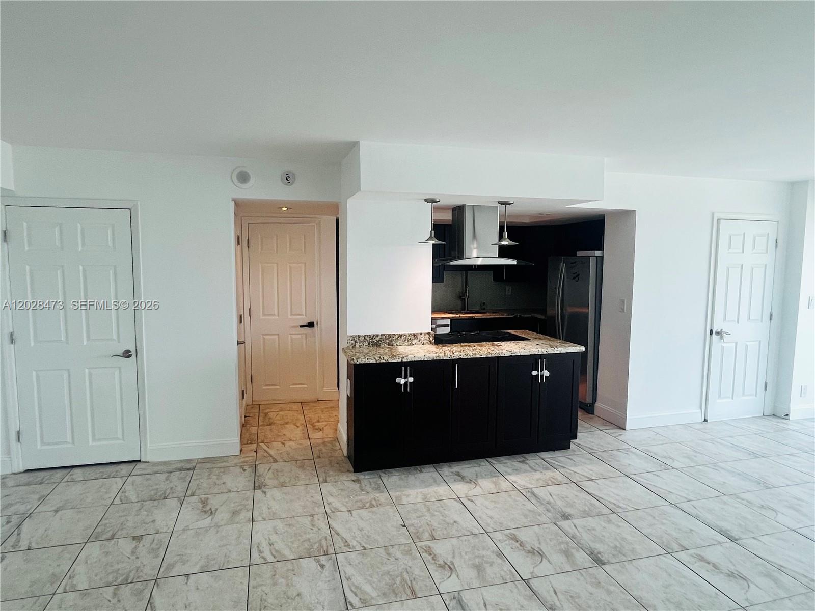 A kitchen with dark cabinets and granite countertops sits between two white interior doors — 2655 Collins Ave # 602, Miami Beach FL 33140, MIAMI BEACH, FL
