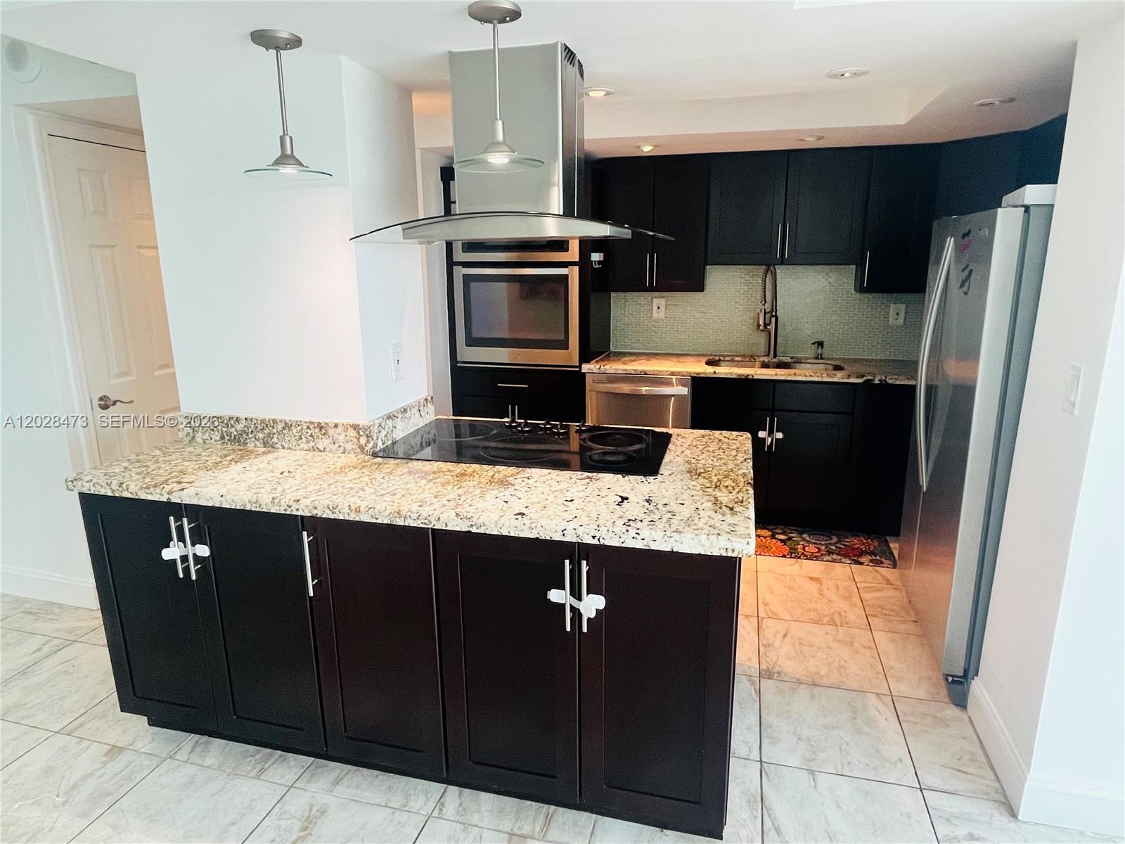 A kitchen features dark cabinetry, granite countertops, a stainless steel range hood, and tile flooring — 2655 Collins Ave # 602, Miami Beach FL 33140, MIAMI BEACH, FL