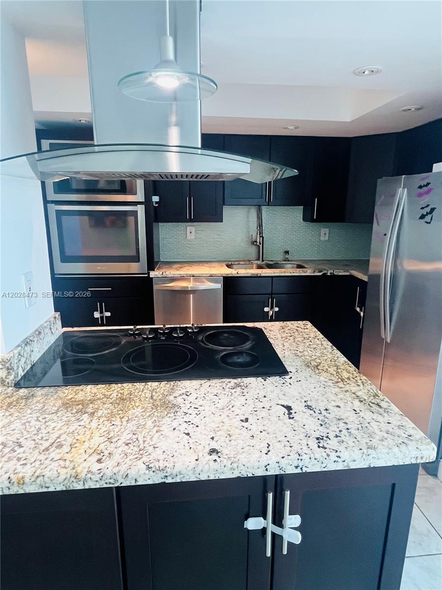A kitchen features dark cabinets, granite countertops, stainless steel appliances, and a central island cooktop — 2655 Collins Ave # 602, Miami Beach FL 33140, MIAMI BEACH, FL