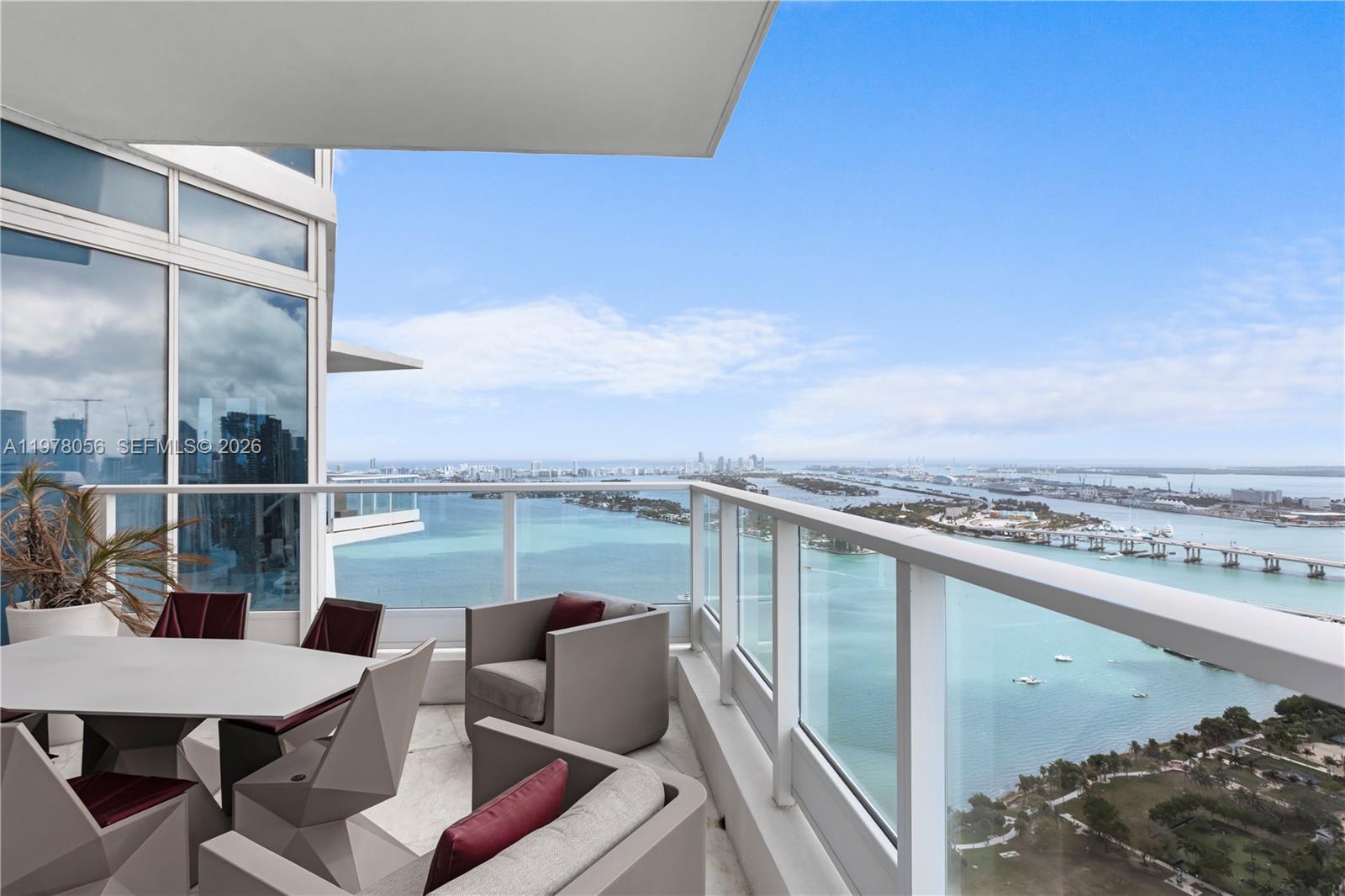 A high-rise balcony features outdoor furniture overlooking a bay with a distant city skyline — 2020 N Bayshore Dr # 4702, Miami FL 33137, MIAMI, FL