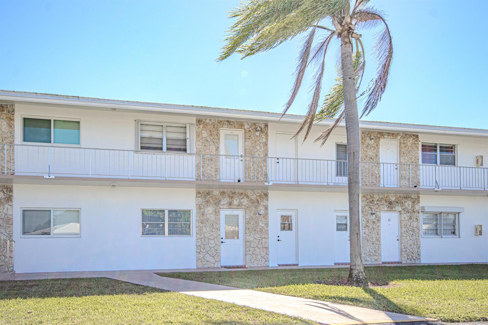 A two-story apartment building with white stucco walls, stone accents, and a palm tree — 2850 W Golf Boulevard # 210, Pompano Beach FL 33064, POMPANO BEACH, FL