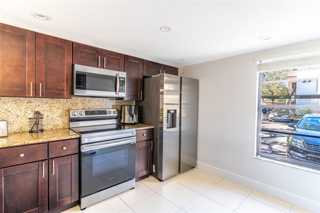 A kitchen features dark wood cabinets, granite countertops, stainless steel appliances, and a window view — 4837 PURITAN CIRCLE UNIT #2505, TAMPA, FL