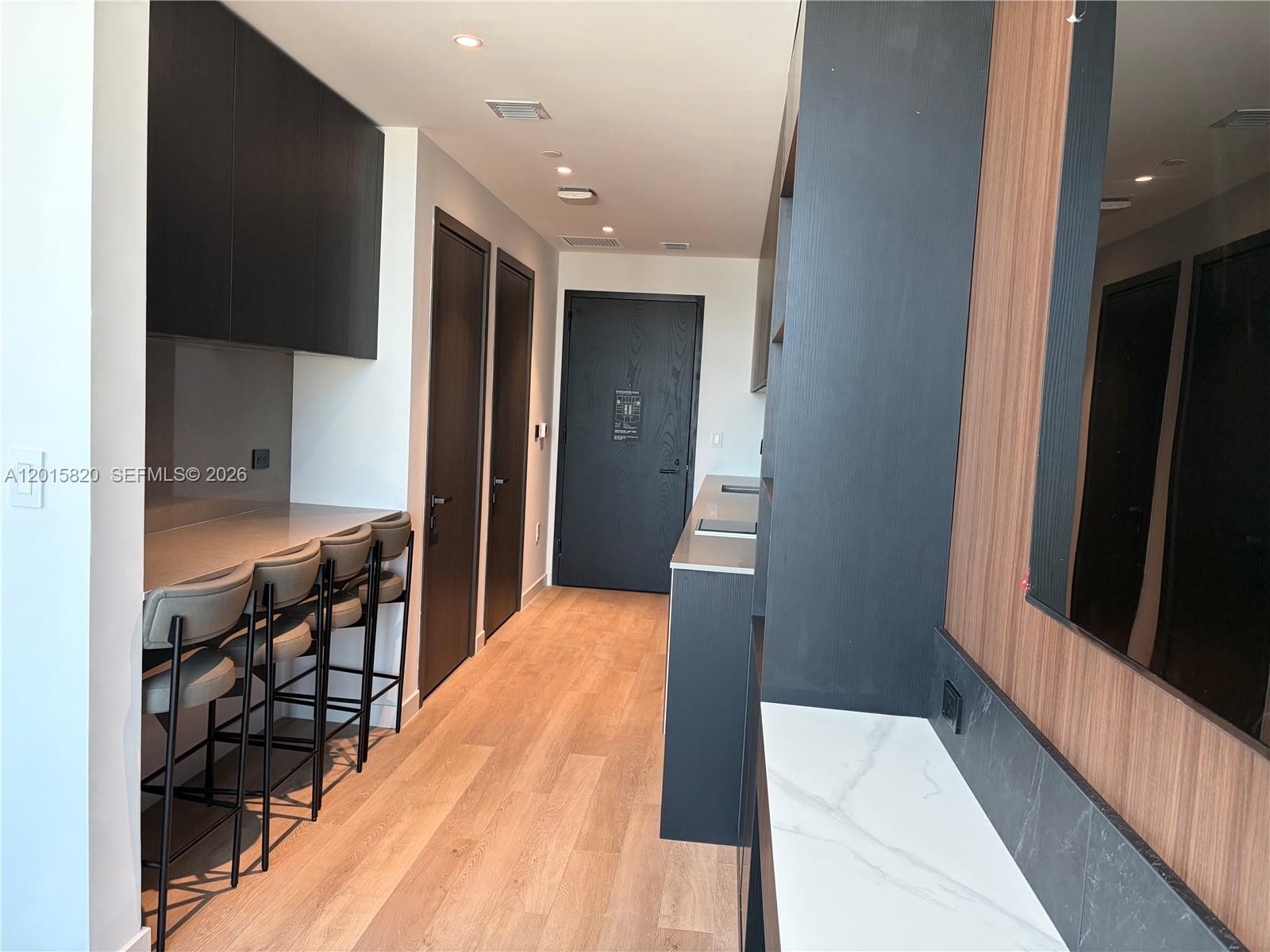 A modern kitchen area features dark cabinetry, a breakfast bar with stools, and wood flooring — 20 ne 11th st # 2805, Miami FL 33132, MIAMI, FL