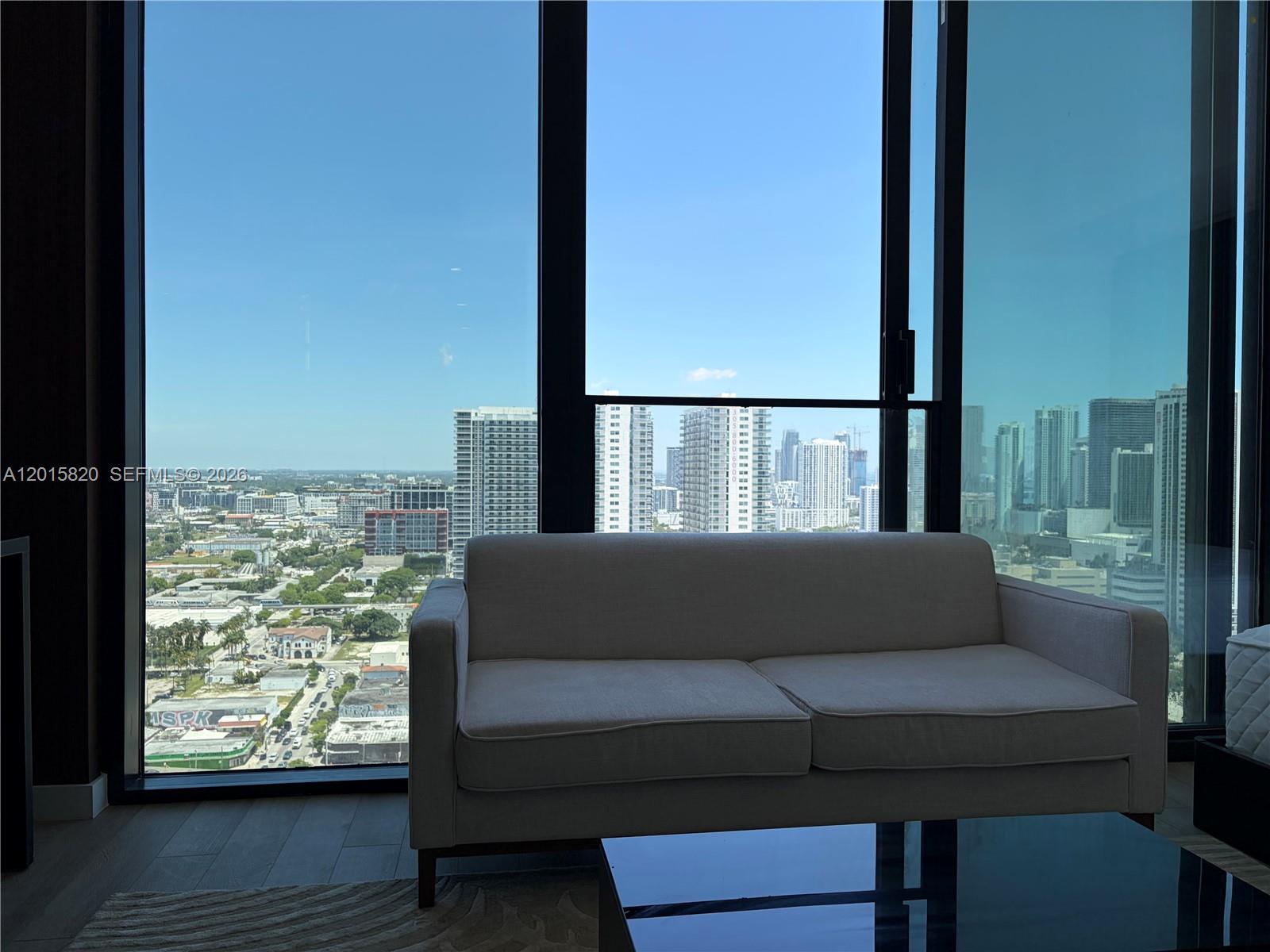 A light-colored sofa sits in a room with floor-to-ceiling windows overlooking a city skyline — 20 ne 11th st # 2805, Miami FL 33132, MIAMI, FL