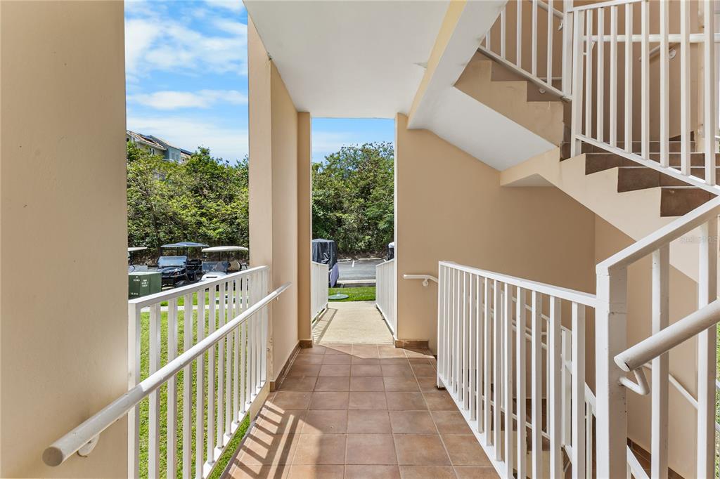 An outdoor tiled walkway features white railings and stairs leading to a parking area — 180 PALMAS DRIVE UNIT 9C, HUMACAO, PR