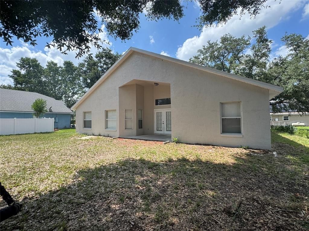 The rear exterior of a beige stucco house features a covered patio and French doors — 2347 BLAKE WAY, OCOEE, FL