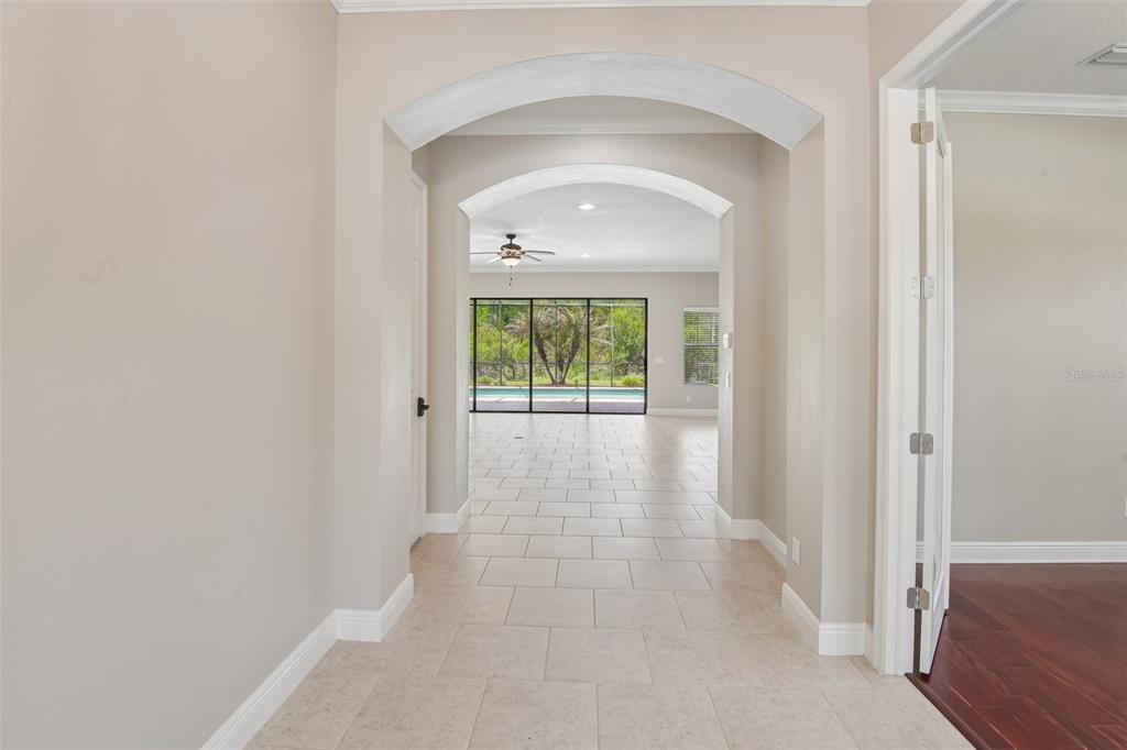 A tiled hallway with arched entryways leads to a living area with a pool view — 8355 SWISS CHARD CIRCLE, LAND O LAKES, FL