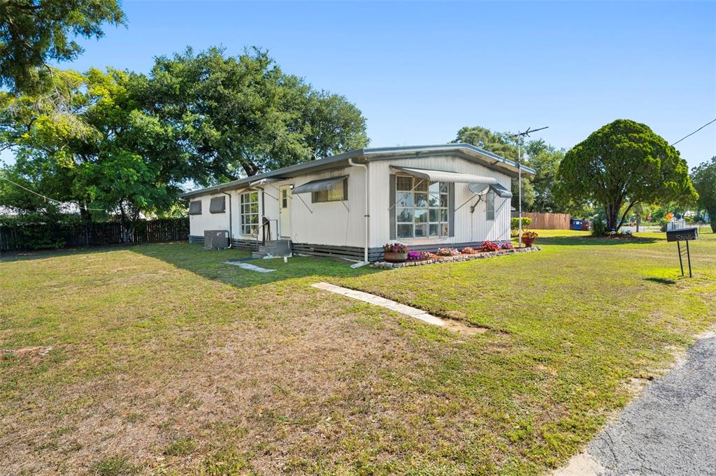 A single-story manufactured home with white siding sits on a grassy lot with trees — 10220 WELLINGTON AVENUE, DADE CITY, FL