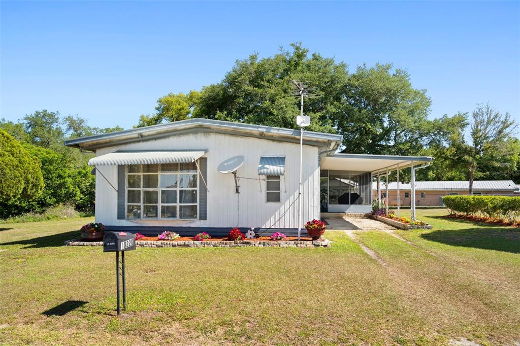 A single-story mobile home with a metal roof, a front porch, and a gravel driveway — 10220 WELLINGTON AVENUE, DADE CITY, FL