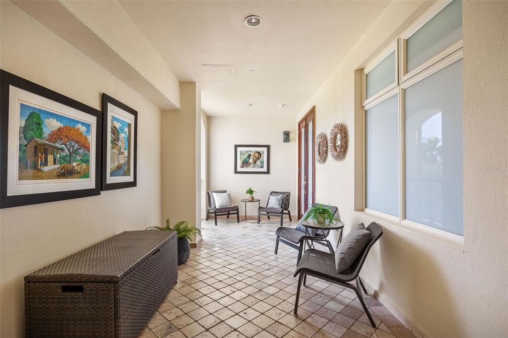 A covered outdoor patio features tiled flooring, wicker furniture, and framed artwork on the walls — 500 PLANTATION VILLAGE DRIVE UNIT 1201, DORADO, PR