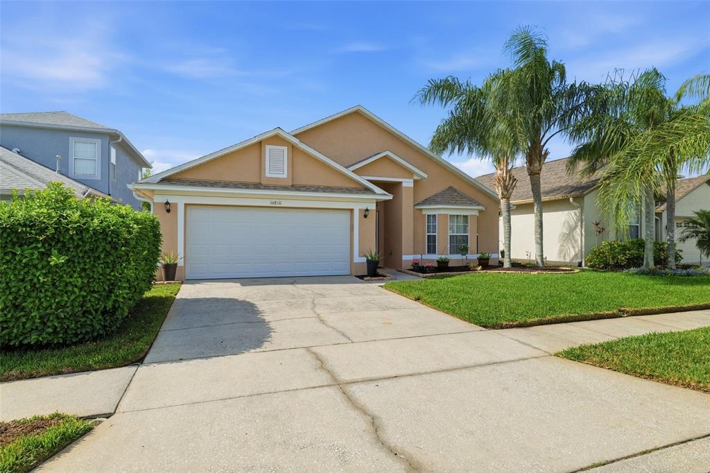 A single-story suburban house with a tan stucco exterior, a two-car garage, and palm trees — 16810 TAYLOW WAY, ODESSA, FL