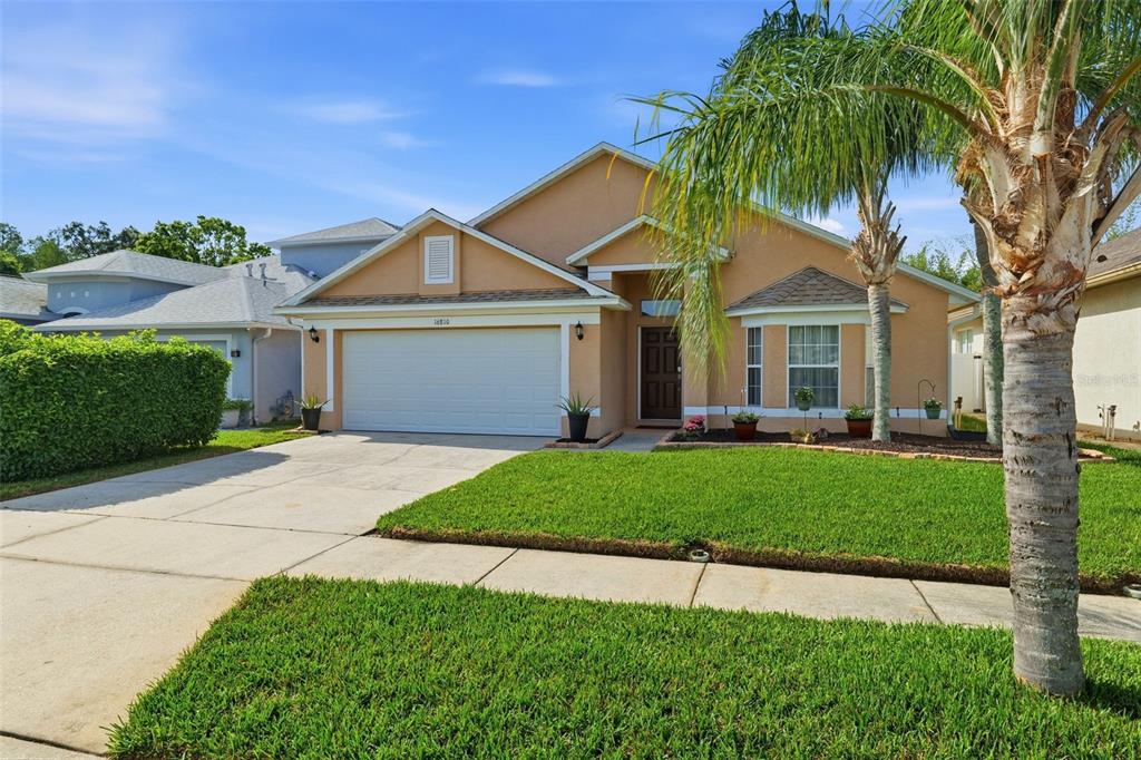 A single-story suburban house with a two-car garage, tan stucco exterior, and a palm tree — 16810 TAYLOW WAY, ODESSA, FL