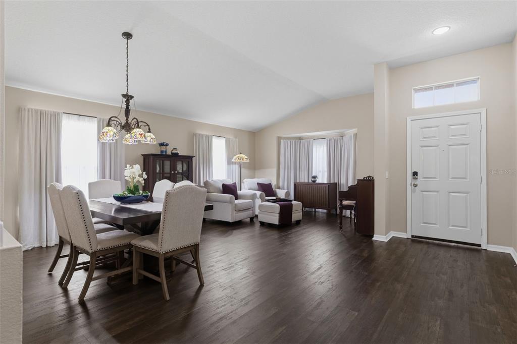 A dining area and living space with dark wood floors, vaulted ceilings, and white furniture — 16810 TAYLOW WAY, ODESSA, FL