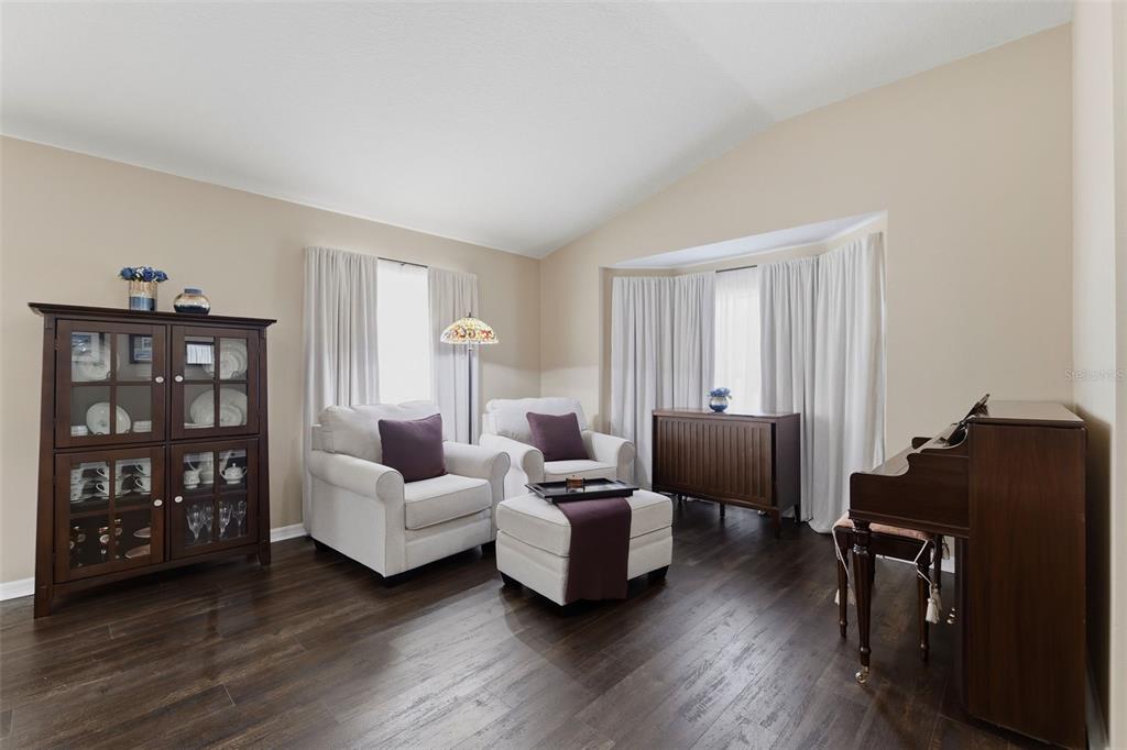 A living room features dark wood floors, two white armchairs, a piano, and a cabinet — 16810 TAYLOW WAY, ODESSA, FL