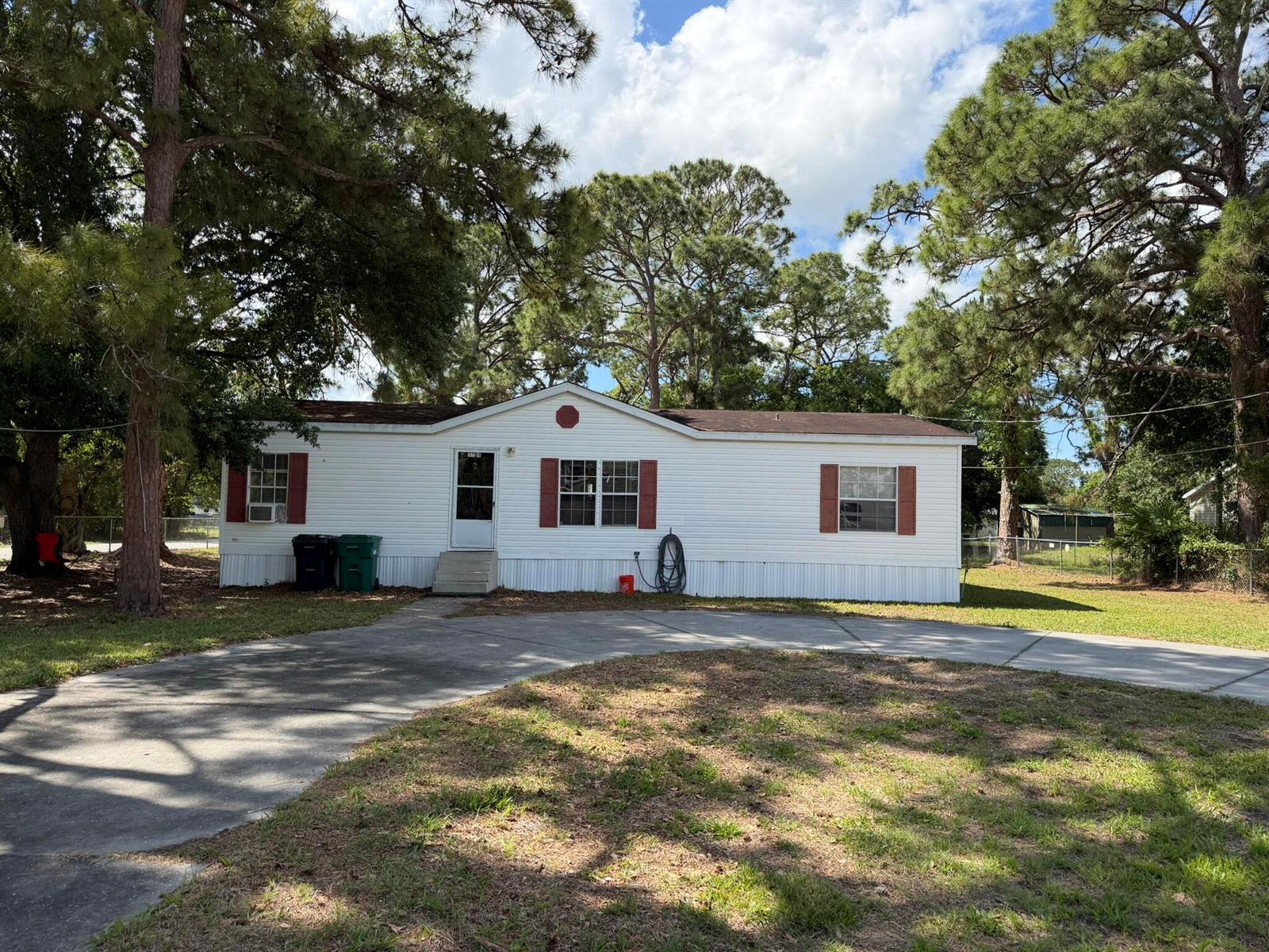 A single-story white manufactured home with red shutters sits behind a concrete driveway — 5924 NE 4th Lane, Okeechobee FL 34974, OKEECHOBEE, FL