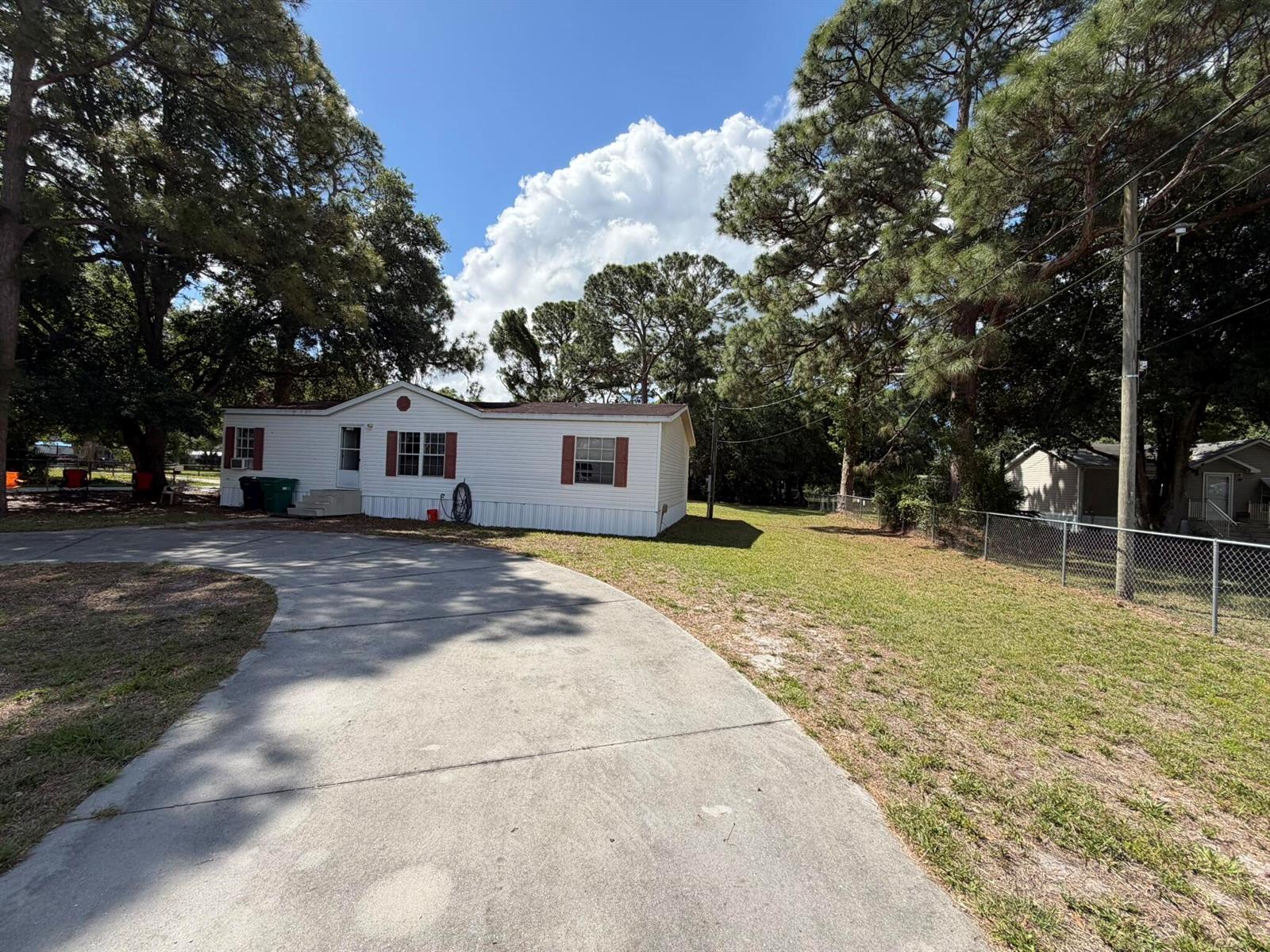 A white single-wide mobile home with red shutters sits on a lot with a concrete driveway — 5924 NE 4th Lane, Okeechobee FL 34974, OKEECHOBEE, FL
